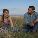 Os dois principais personagens do filme sentados no campo, olhando um para o outro.