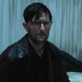 O ator Adam Scott expressando tensão em uma cena escura do filme Hokum.
