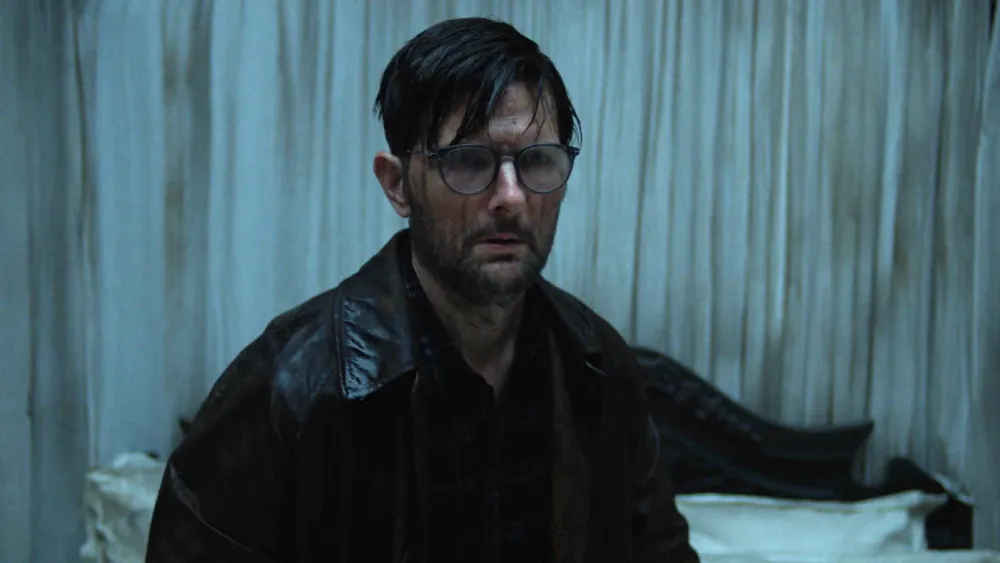 O ator Adam Scott expressando tensão em uma cena escura do filme Hokum.