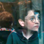 Harry Potter olhando para rua de dentro de um trem.