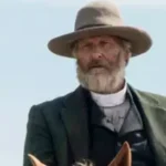 O ator Jeff Daniels sorrindo em um evento de tapete vermelho, vestindo um terno escuro.