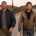 Kyle Chandler e Aaron Pierre caminham por uma estrada deserta na série Lanternas.