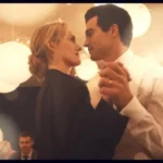 Dois atores caracterizados como o casal Kennedy em um ambiente urbano iluminado com tons quentes de Nova York.