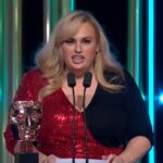 A atriz Rebel Wilson em um tapete vermelho sorrindo para fotógrafos.