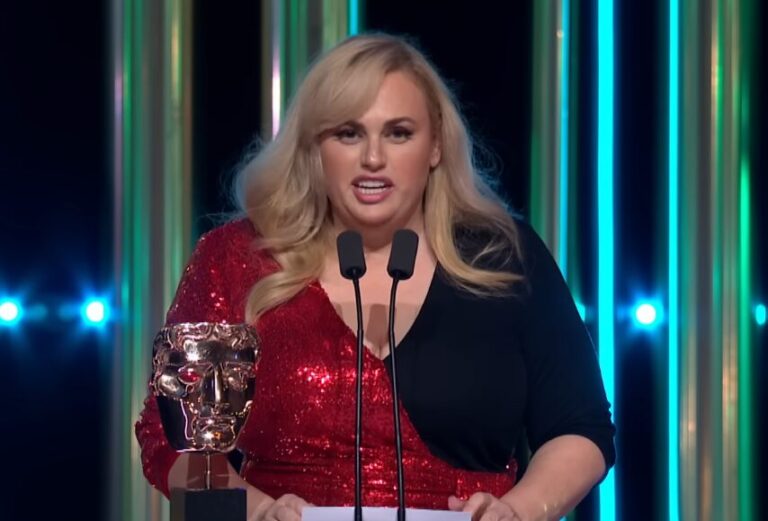 A atriz Rebel Wilson em um tapete vermelho sorrindo para fotógrafos.