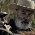 O ator Alec Baldwin caracterizado para o filme Rust: A Lei do Oeste, vestindo trajes de época em um cenário de faroeste.