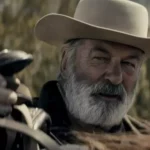 O ator Alec Baldwin caracterizado para o filme Rust: A Lei do Oeste, vestindo trajes de época em um cenário de faroeste.