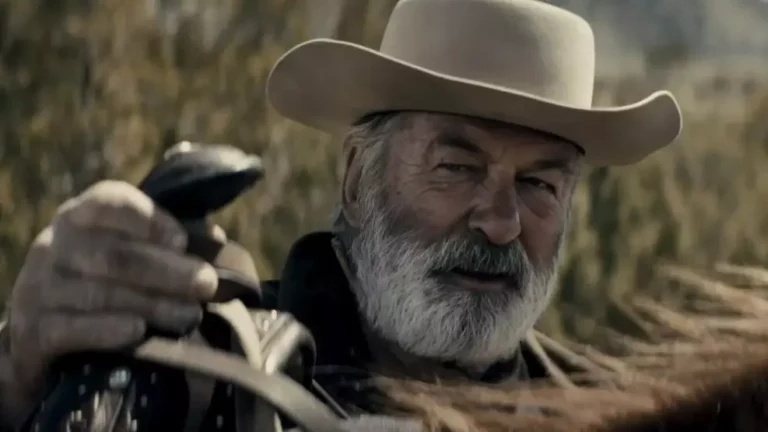 O ator Alec Baldwin caracterizado para o filme Rust: A Lei do Oeste, vestindo trajes de época em um cenário de faroeste.