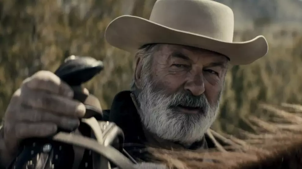 O ator Alec Baldwin caracterizado para o filme Rust: A Lei do Oeste, vestindo trajes de época em um cenário de faroeste.