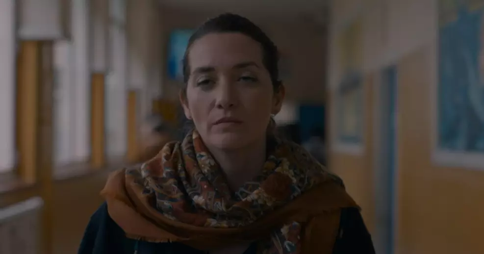 Atriz Selma Alaoui em cena do filme Aquela Noite, usando um cachecol estampado e encarando a câmera com expressão séria em um corredor subexposto.