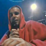 Justin Bieber no palco do Coachella cantando em frente a um notebook em uma estrutura simples.