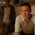 Millie Bobby Brown aparece com semblante sério e preocupado em cena de produção da Netflix, vestindo roupa esportiva em ambiente fechado.