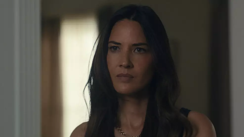 Olivia Munn em entrevista durante programa de TV, relatando bastidores de gravação com colega de elenco em cena de ação.