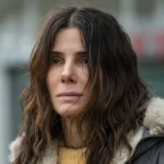 Sandra Bullock sorrindo em evento de divulgação do filme Da Magia à Sedução 2, vestindo blazer escuro e camisa branca.