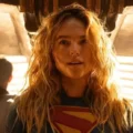 A atriz Milly Alcock caracterizada como Supergirl em um cenário espacial vasto.