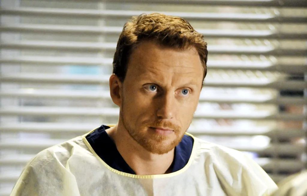 Owen Hunt com expressão severa em um laboratório médico, instruindo residentes de Grey's Anatomy sobre o polêmico treinamento prático com porcos.