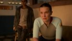 Millie Bobby Brown aparece com semblante sério e preocupado em cena de produção da Netflix, vestindo roupa esportiva em ambiente fechado.