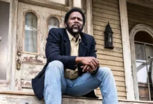 Cena sombria de Origem mostra personagem em cidade misteriosa cercada por floresta